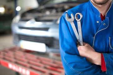 Auto shop worker holding tools and preparing to perform service repairs on a vehicle