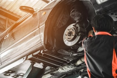 Auto shop technician working in the wheel well of a vehicle that's raised on a lift